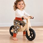 Petite fille de dix-huit mois à califourchon sur une draisienne en bois, portant un sarouel évolutif fleuri avec des bandes terracotta.