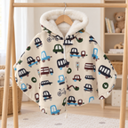 Poncho pour enfant à fond crème et motifs de véhicules, suspendu sur un portant en bois, avec capuche doublée de fourrure blanche.