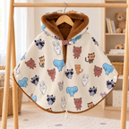 Poncho pour enfant à fond crème et motifs de petits animaux colorés, suspendu sur un portant en bois, avec capuche doublée de fourrure brune.