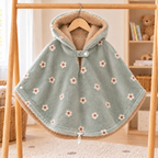 Poncho pour enfant vert sauge à petites fleurs crème et vieux rose, suspendu sur un portant en bois, avec capuche doublée de fourrure beige.