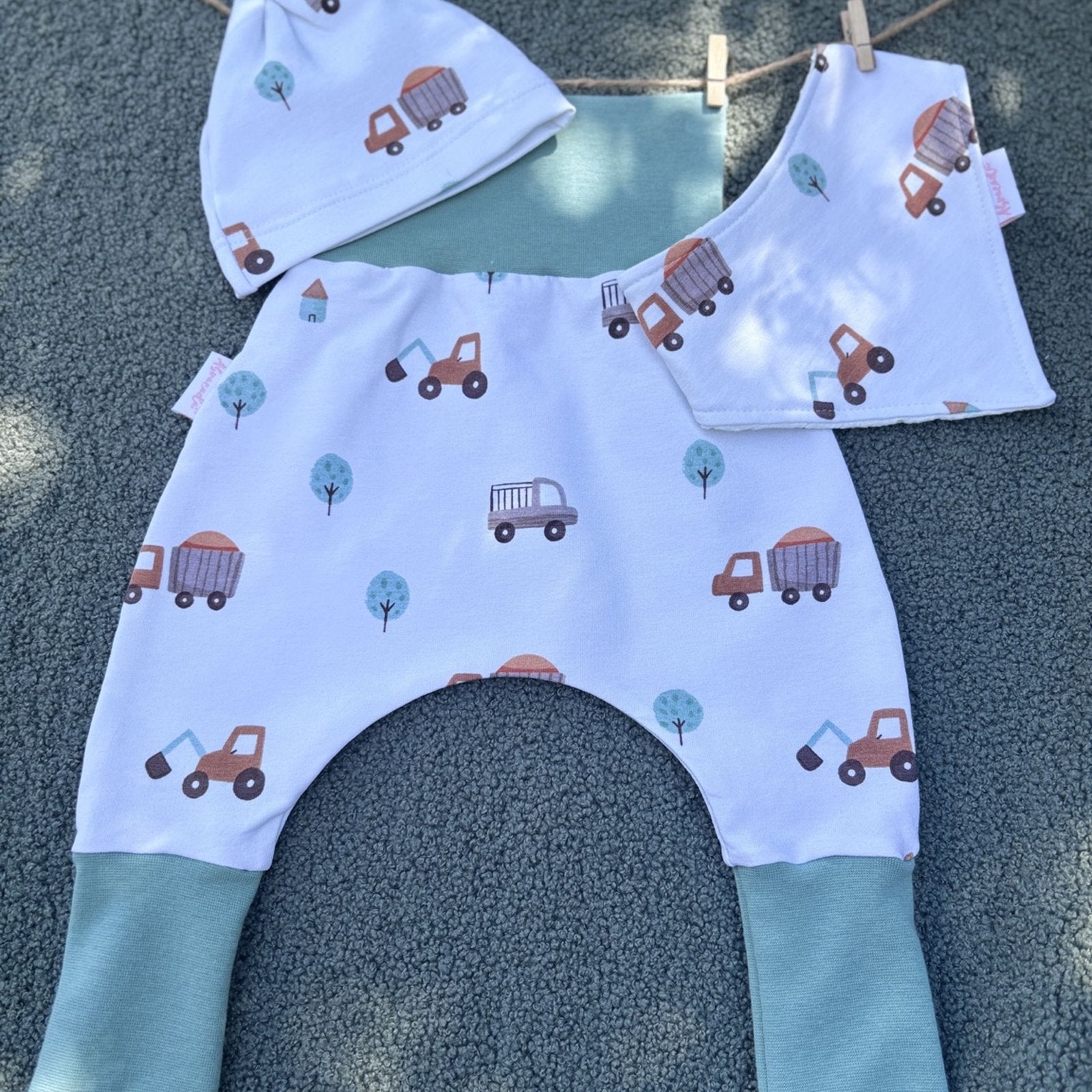 Vue de dessus de l’ensemble naissance motif chantier – bonnet, bavoir et sarouel bébé faits main