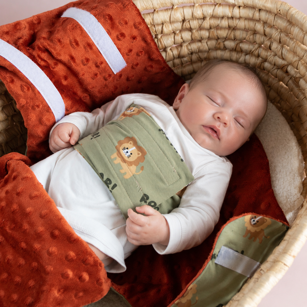 Bébé endormi dans un cocon d’emmaillotage motif lions “ROAR!” dans un panier en osier.