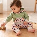 Bébé de dix mois jouant avec une voiture en bois, en sweat sauge et sarouel rose clair à feuilles.