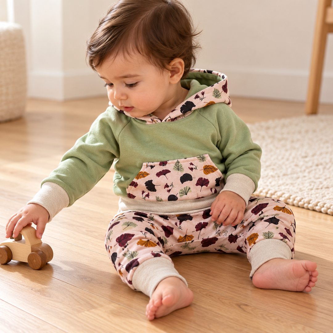 Bébé de dix mois jouant avec une voiture en bois, en sweat sauge et sarouel rose clair à feuilles.