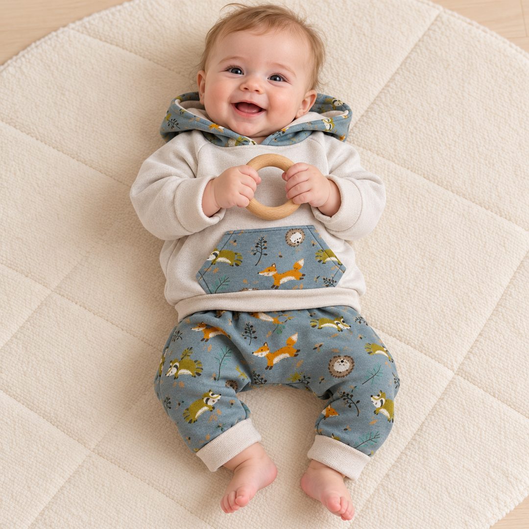 Bébé de six mois allongé sur un tapis, portant un sweat écru et un sarouel bleu grisé à animaux.