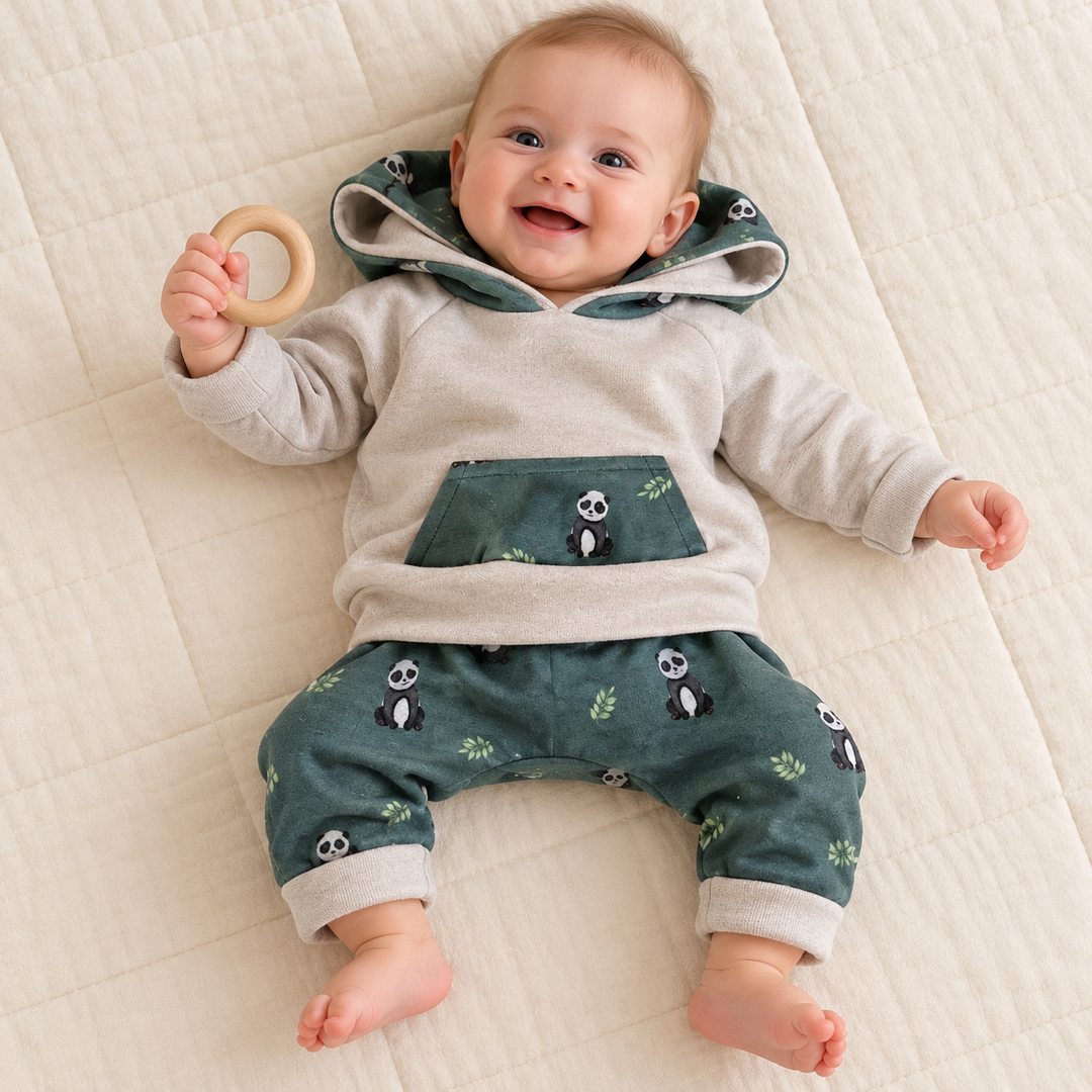 Bébé de six mois allongé avec un anneau, portant un sweat écru et un sarouel vert à pandas, bords repliés.