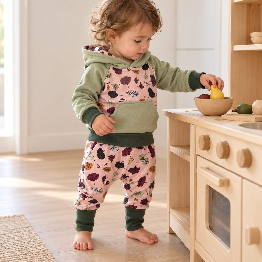 Enfant de dix-huit mois jouant à la cuisine, en sweat sauge à empiècement feuillage et sarouel assorti à bords vert forêt.
