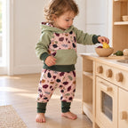 Enfant de dix-huit mois jouant à la cuisine, en sweat sauge à empiècement feuillage et sarouel assorti à bords vert forêt.