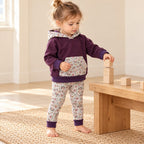 Enfant de deux ans empilant des cubes, vêtu d’un sweat prune et d’un legging clair à petites fleurs, bords repliés.