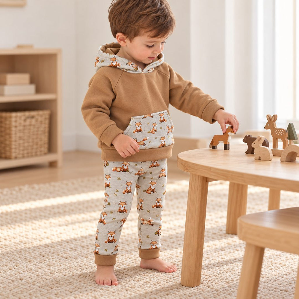 Garçon de deux ans jouant avec des animaux en bois, en sweat camel et legging gris à renards, bords repliés.