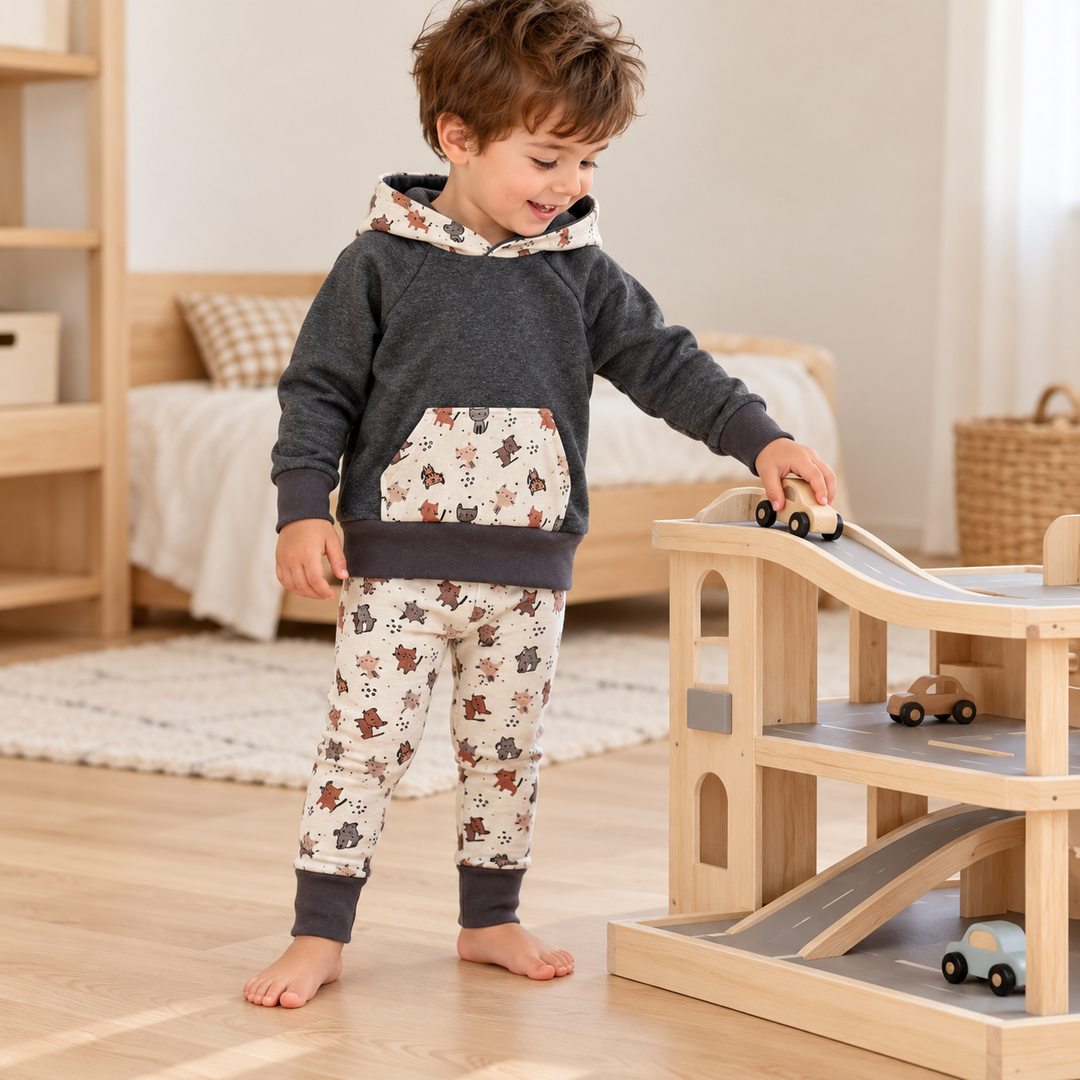 Garçon de trois ans jouant avec un garage en bois, vêtu d’un sweat anthracite et d’un legging écru à chats, bords dépliés.