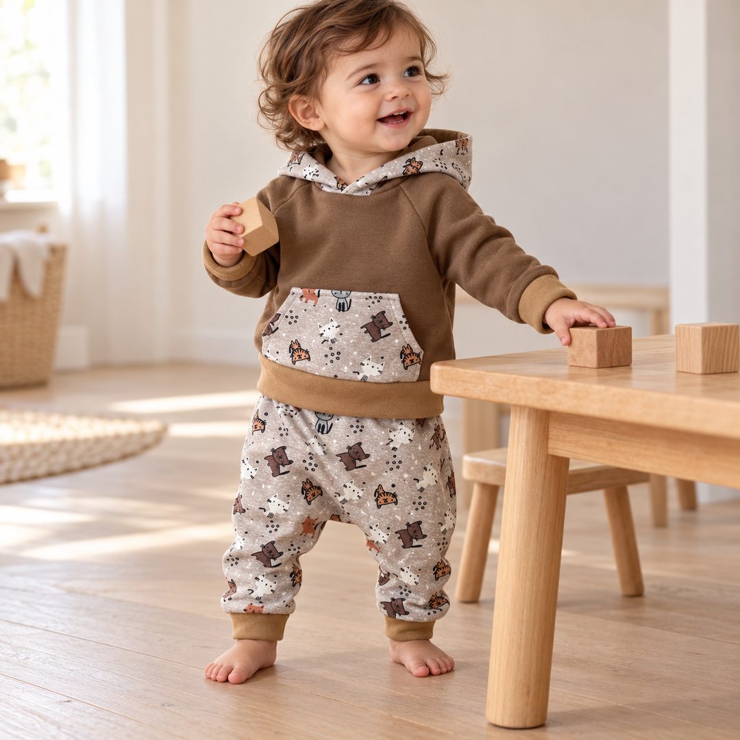 Enfant d’un an jouant avec des cubes, vêtu d’un sweat brun à capuche et d’un sarouel gris à petits chats.