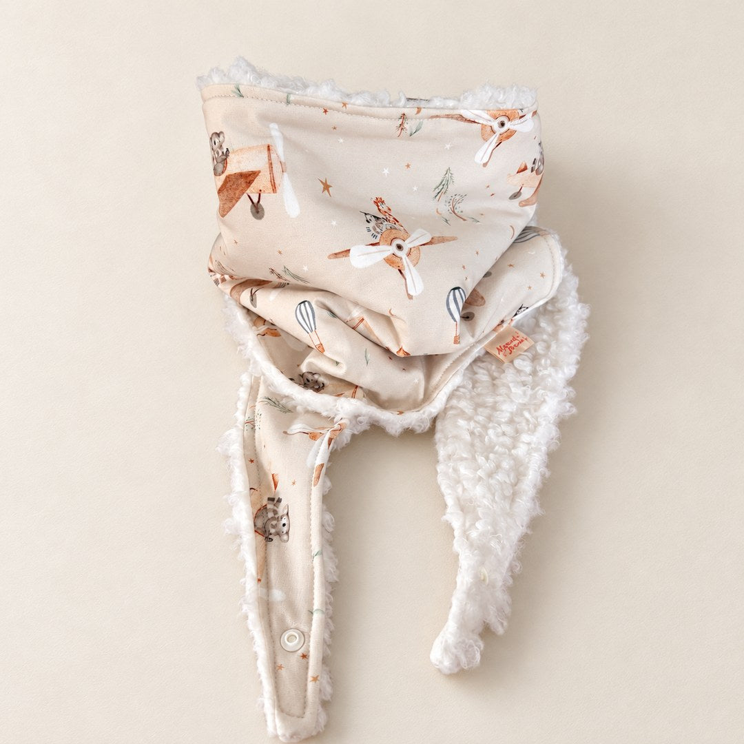 Foulard enfant beige à motifs d’animaux aviateurs, d’avions et de montgolfières, avec doublure blanche, présenté sur fond crème.