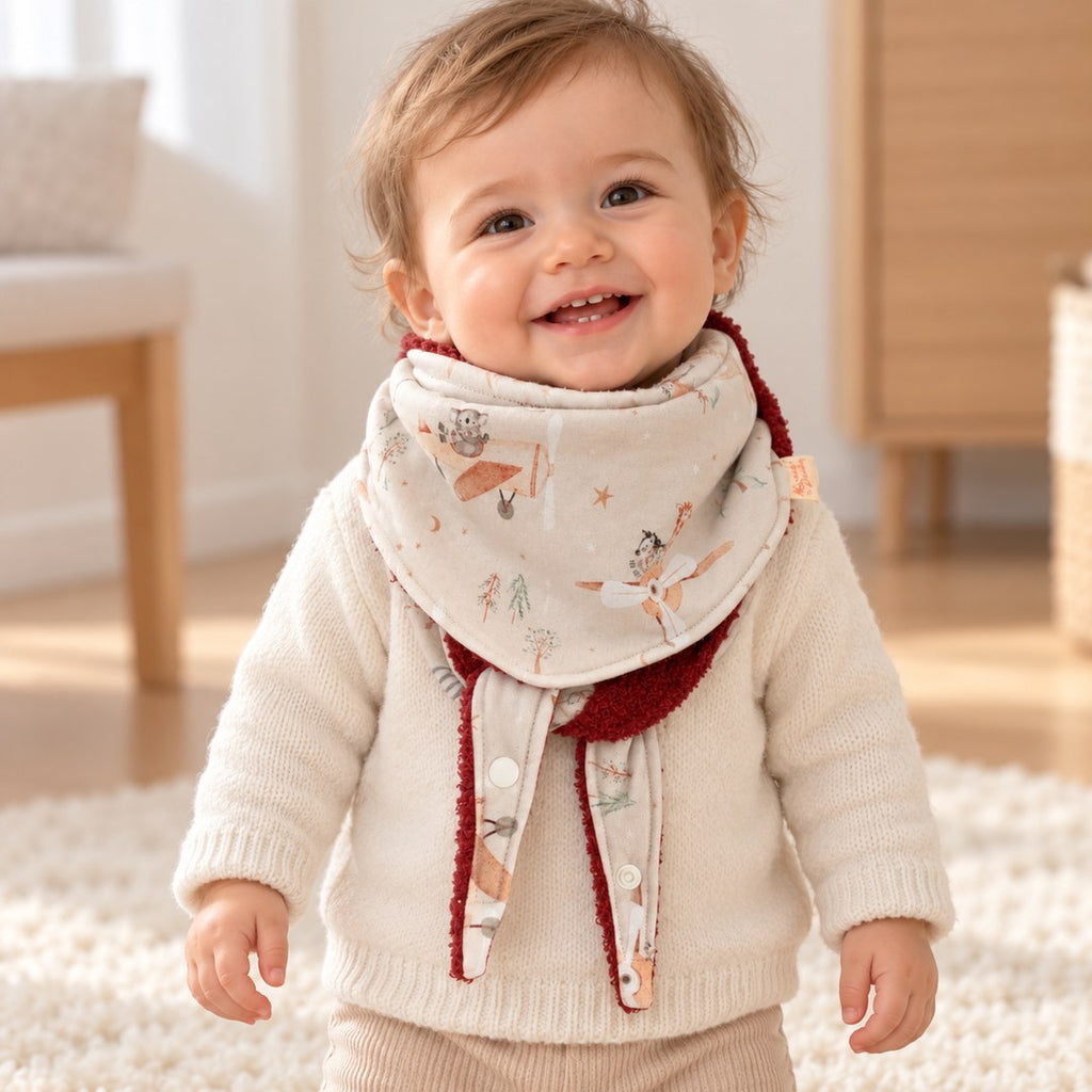 Foulard enfant à motifs d’animaux aviateurs, avec doublure rouille foncé, porté par un bébé.