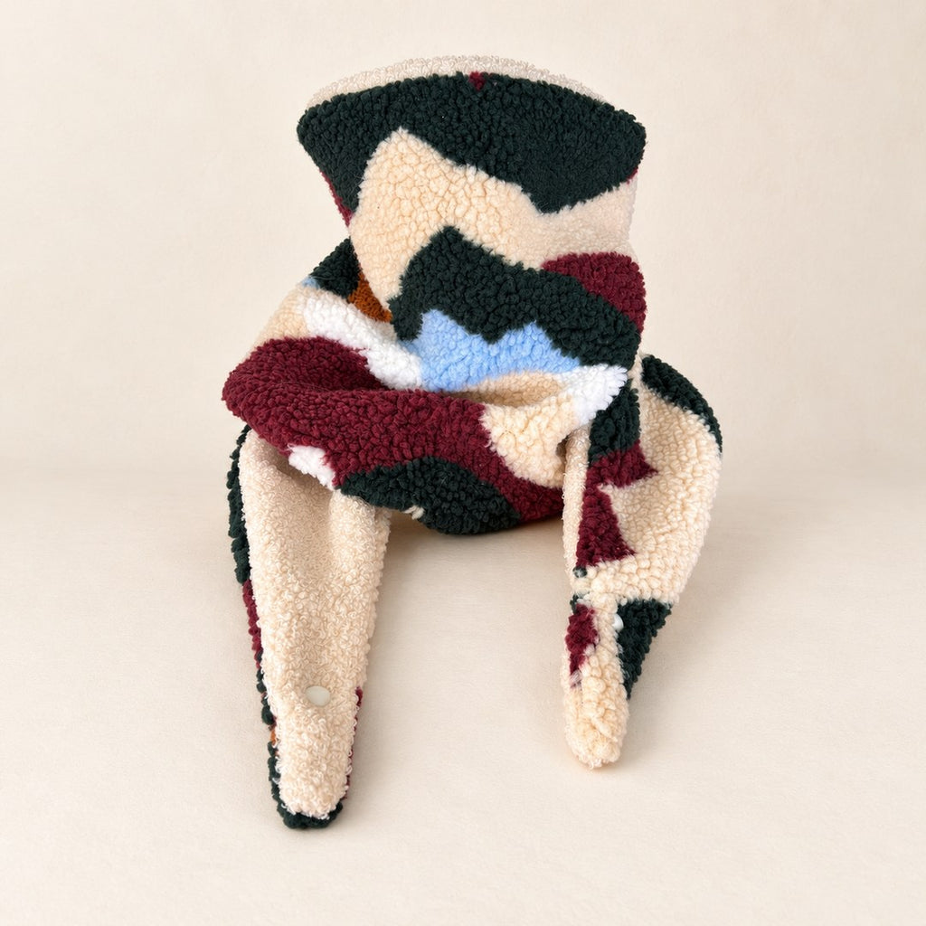 Foulard enfant en tissu bouclé à formes vert forêt, bordeaux, crème et bleu clair, avec doublure beige, présenté sur fond crème.