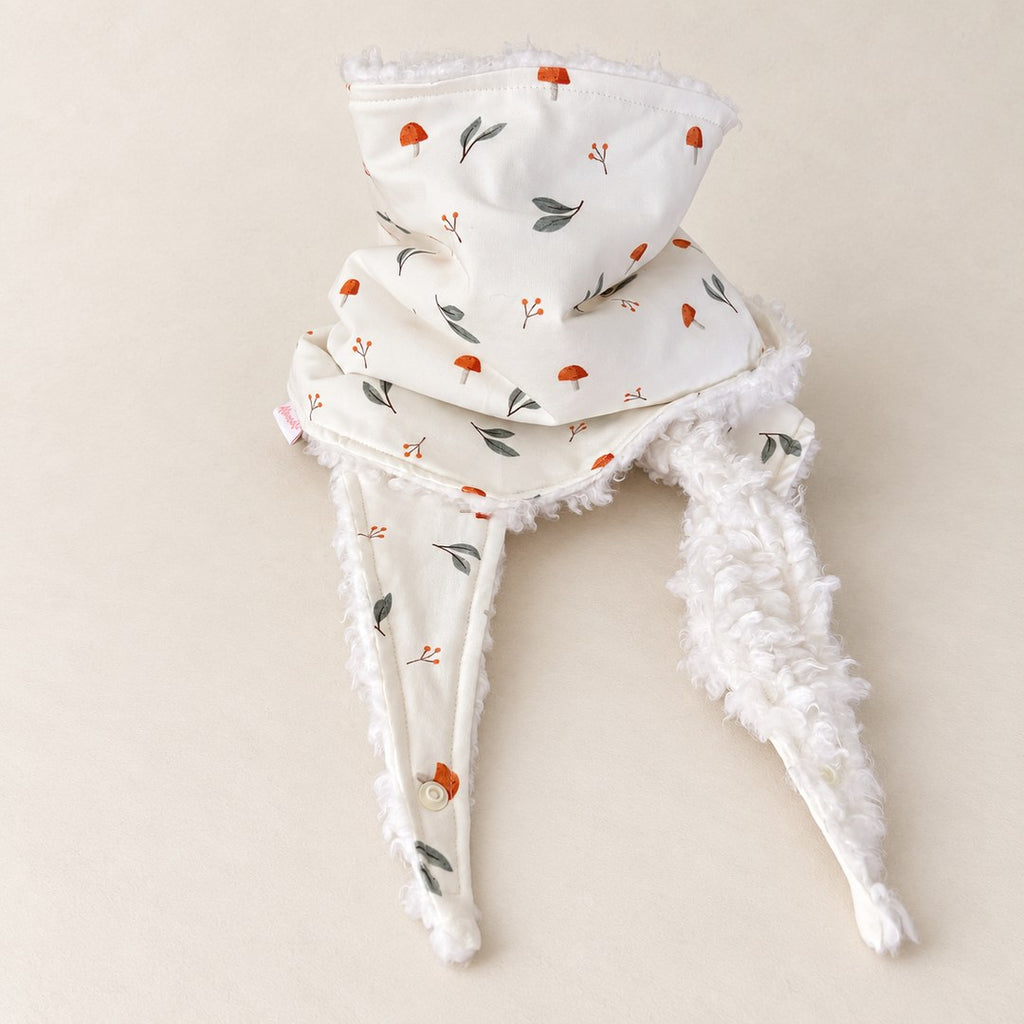 Foulard enfant écru à motifs de champignons orange et de feuilles vert gris, avec doublure blanche, présenté sur fond crème.