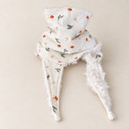 Foulard enfant écru à motifs de champignons orange et de feuilles vert gris, avec doublure blanche, présenté sur fond crème.