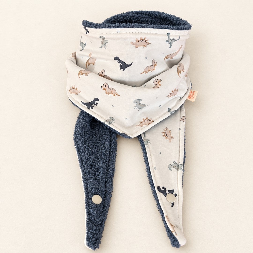 Foulard enfant écru à motifs de petits dinosaures, avec doublure bleu gris et deux pans ouverts, présenté sur fond crème.