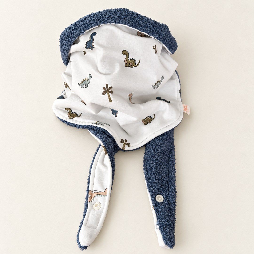 Foulard enfant écru à motifs de dinosaures à long cou et de palmiers, avec doublure bleu gris, présenté sur fond crème.