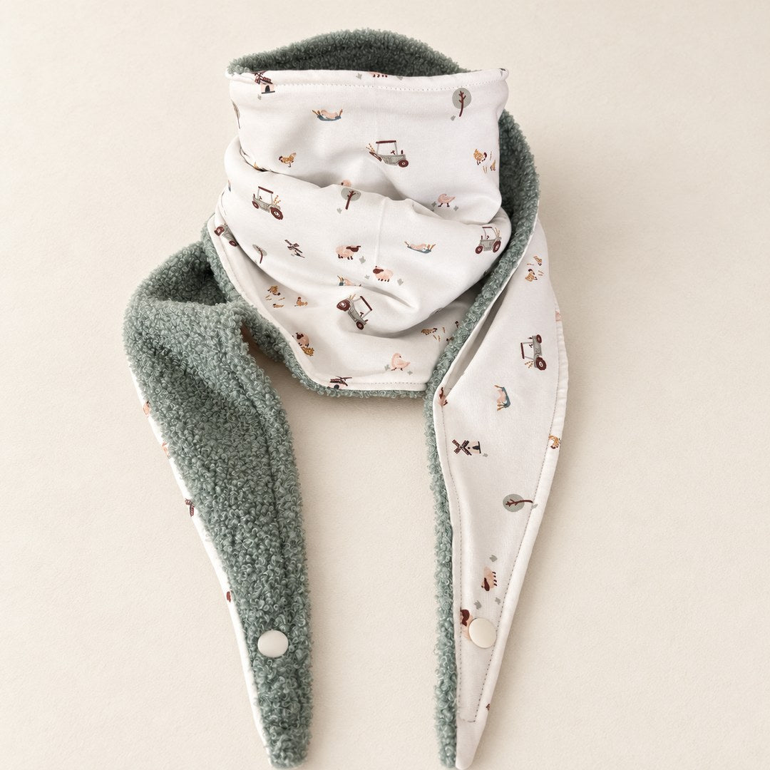 Foulard enfant écru à motifs de petits tracteurs et d’animaux de ferme, avec doublure vert sauge, présenté sur fond crème.