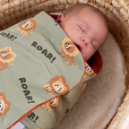 Gros plan d’un bébé dormant dans un cocon d’emmaillotage motif lion vert sauge.
