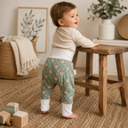 Bébé souriant portant un pantalon évolutif vert à motifs léopard dans une ambiance douce et naturelle.