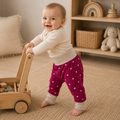 Bébé debout avec pousseur en bois portant un pantalon évolutif fuchsia à petits cœurs