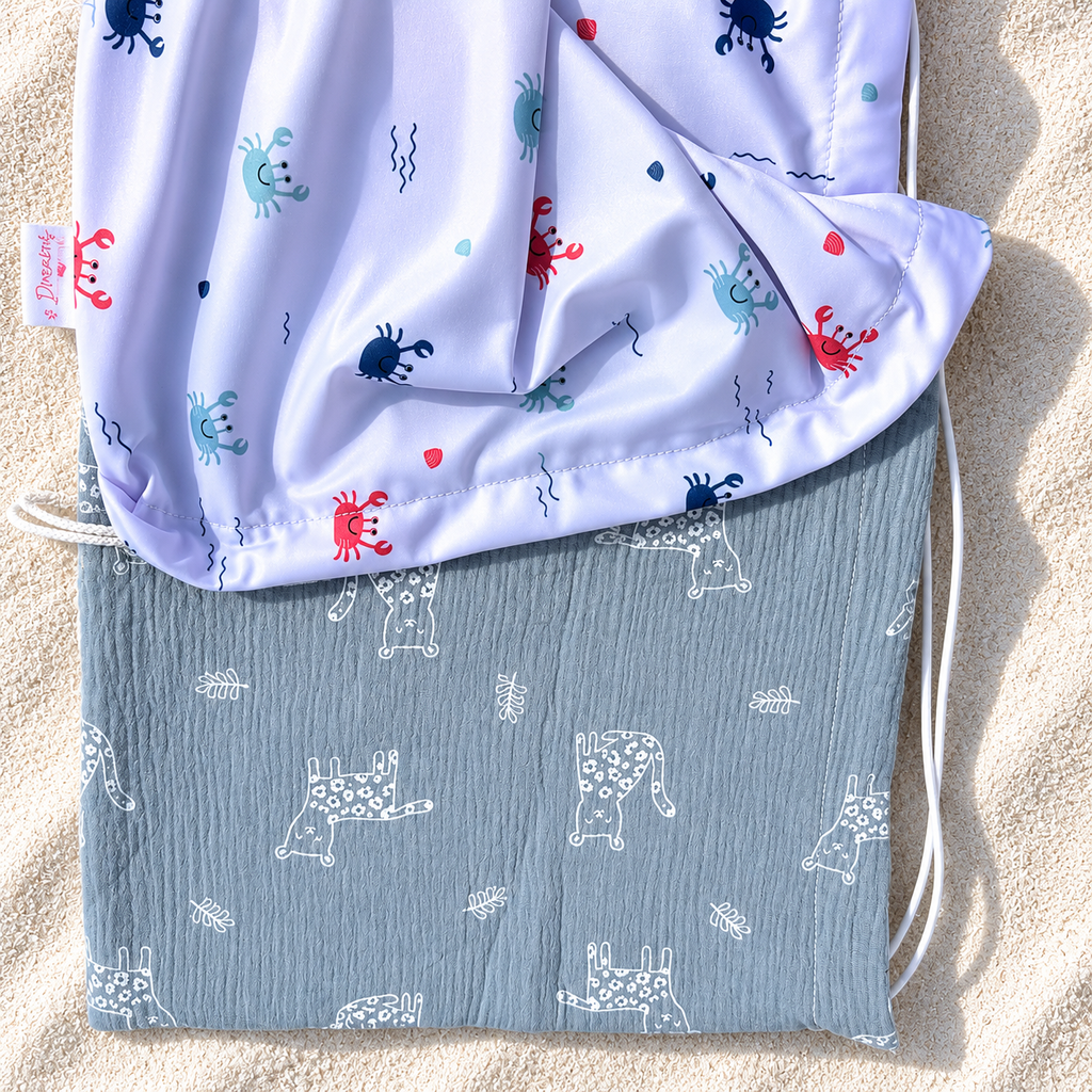 Pare-soleil pour poussette motif crabes avec double gaze grise posé sur du sable blanc
