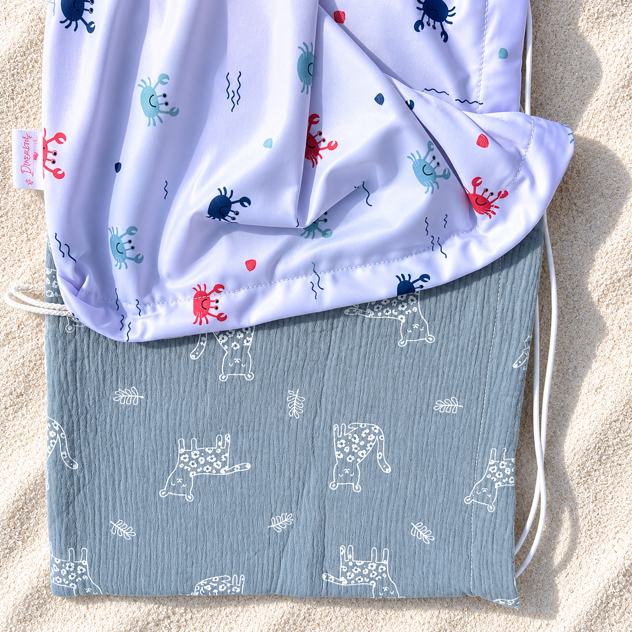 Pare-soleil pour poussette motif crabes avec double gaze grise posé sur du sable blanc