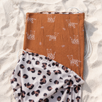 Pare-soleil pour poussette terracotta avec motifs félins et tissu léopard posé sur une plage de sable blanc