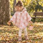 Petite fille d’environ quatre ans jouant dans un parc avec un poncho rose à motifs de lapins et de carottes. Ses mains dépassent des ouvertures formées par les pressions latérales fermées.