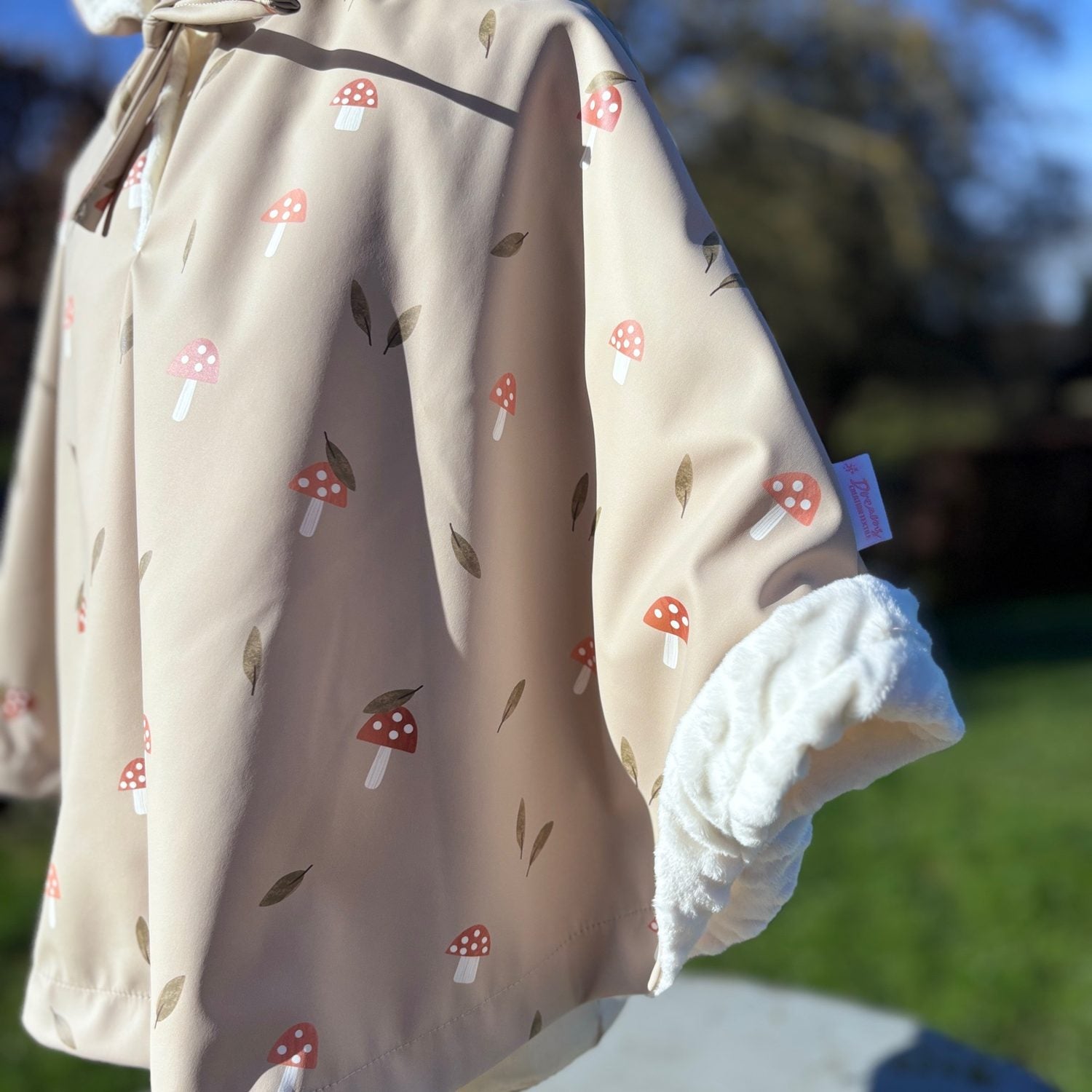 Détail manche du poncho de pluie enfant imprimé champignons : finition doublée minky blanc et étiquette Abracada Dreams.