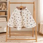 Poncho de siège auto écru à petits motifs de zèbres, éléphants et tortues, avec capuche doublée de fourrure douce, sur un portant en bois.