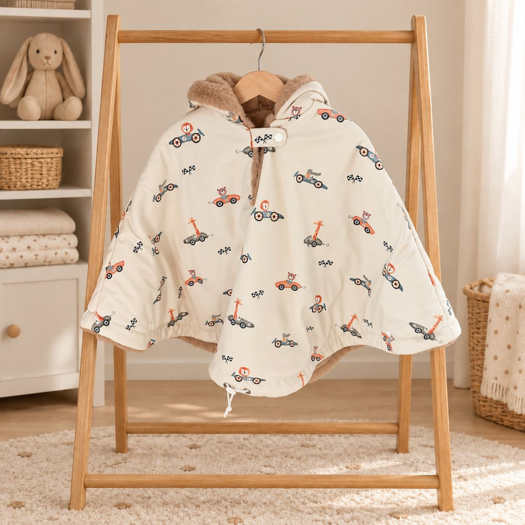 Poncho de siège auto écru à motifs de petites voitures de course et de drapeaux, avec capuche doublée de fourrure douce, sur un portant en bois.