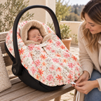 Bébé installé dans un Maxi-Cosi, enveloppé d’un poncho fleuri à capuche doublée de fourrure beige. Sa maman, assise à côté, tient le cordon de serrage au bas du poncho.