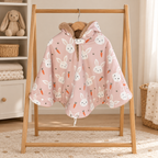 Poncho de siège auto rose à motifs de lapins blancs et de carottes, avec capuche doublée de fourrure douce, suspendu à un portant en bois.