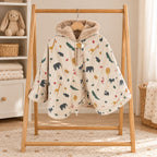 Poncho de siège auto beige à motifs d’animaux safari, dont des girafes, éléphants et crocodiles, avec capuche doublée de fourrure douce, sur un portant en bois.