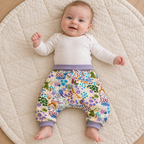 Bébé de trois mois portant un sarouel évolutif à motifs d’animaux et de fleurs, avec les bandes mauves repliées à la taille et aux chevilles.