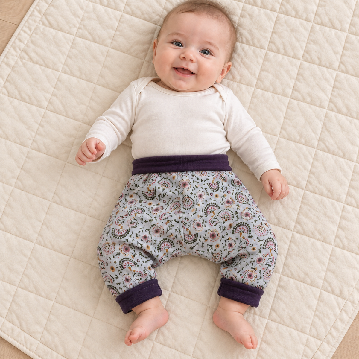 Sarouel évolutif à petits motifs fleuris porté par un bébé de trois mois, avec la taille et les chevilles violet foncé entièrement repliées.