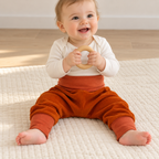 Bébé assis jouant avec un jouet en bois, vêtu d’un sarouel évolutif orange en velours côtelé avec de longues bandes aux chevilles.